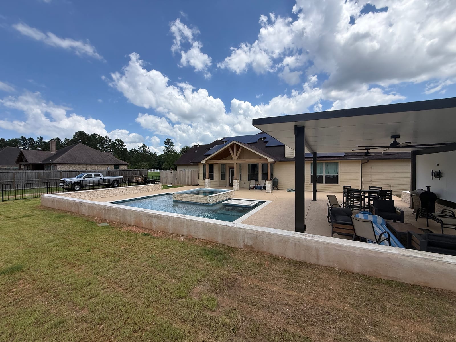 Raised pool and spa with a timber pergola and covered patio across an open lawn
