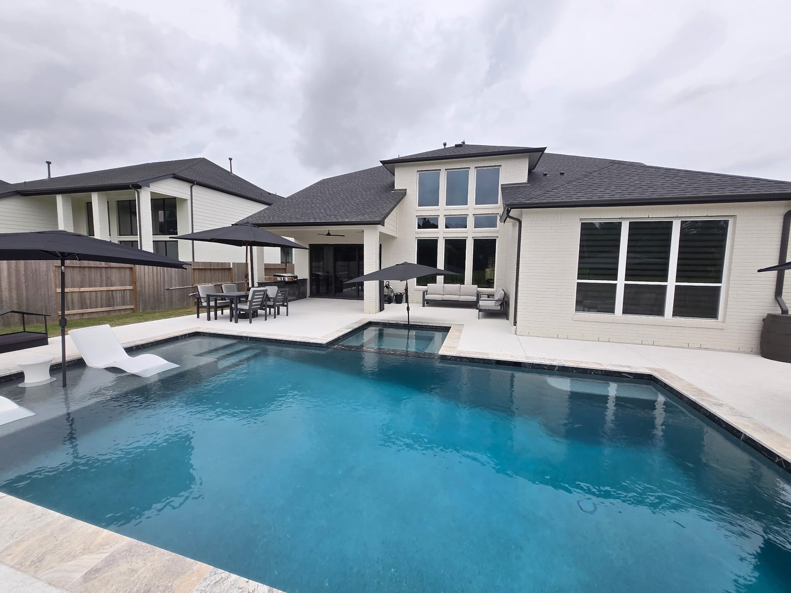Geometric gunite pool with a raised spa and turquoise water behind a white brick home