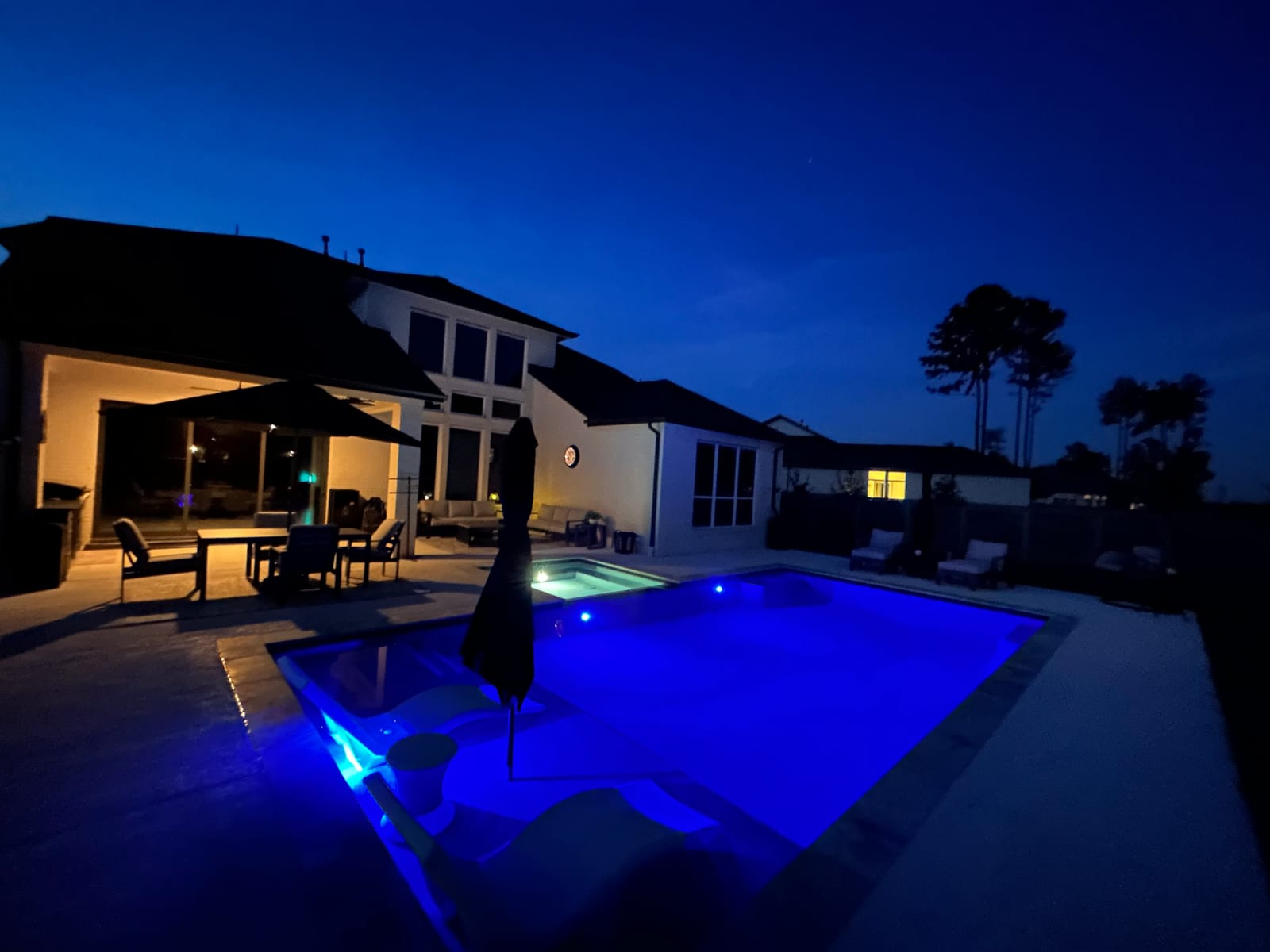 Pool lit bright blue at dusk with the house and covered patio glowing behind it