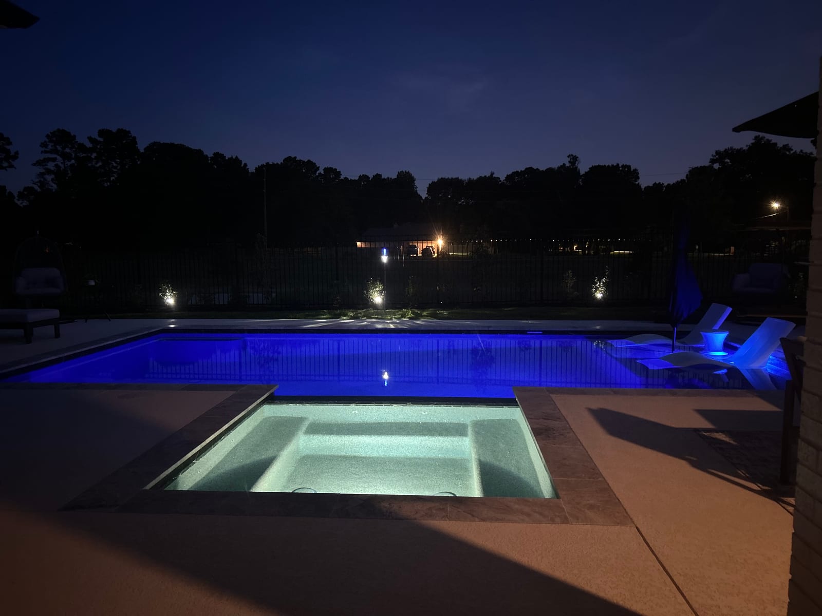 Wide night view of the lit pool and spa with the deck in darkness